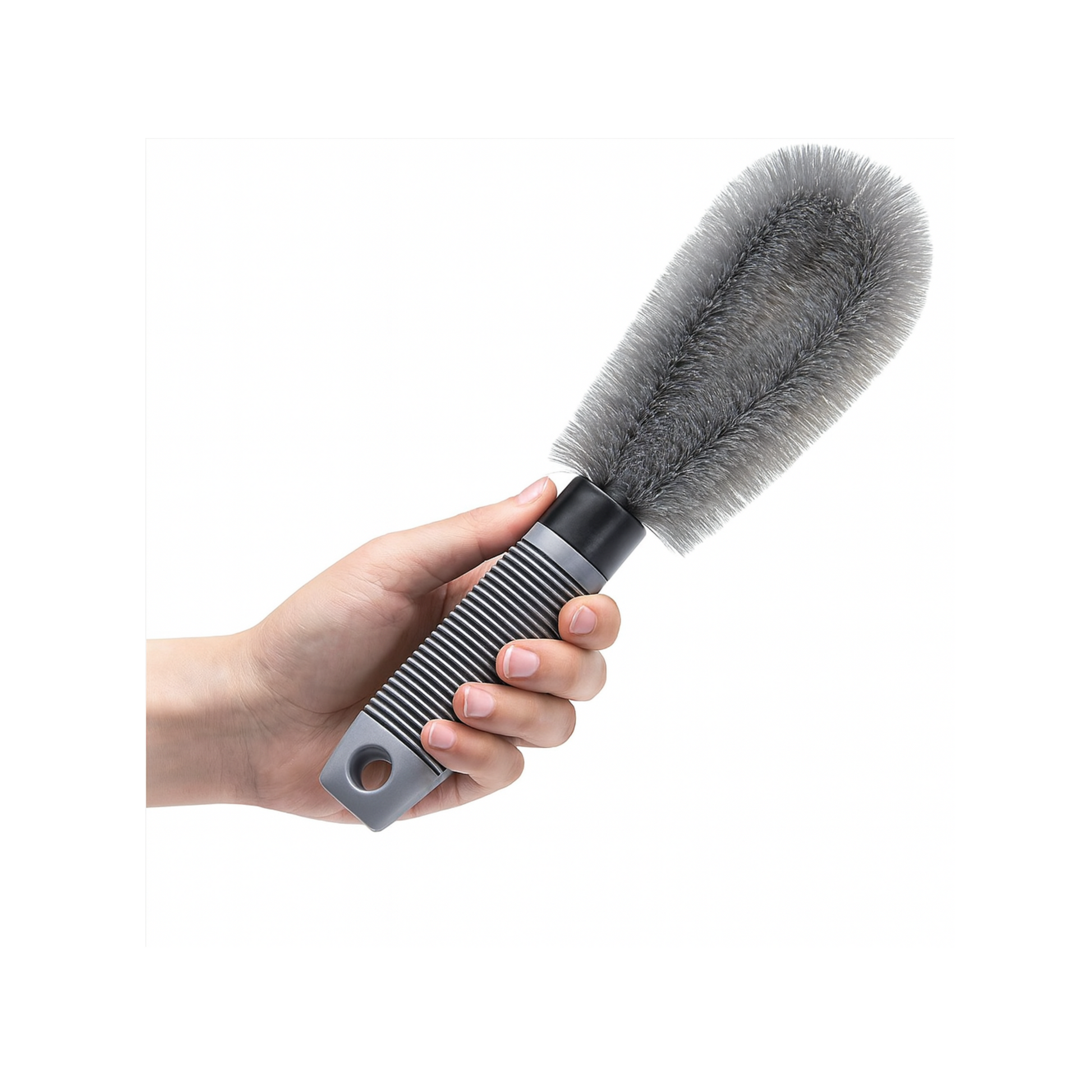 Hand holding a cleaning brush with a gray bristle head and black handle on a white background
