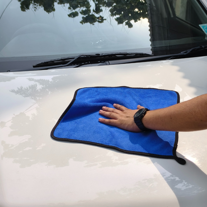 Person cleaning a car with a blue microfiber towel on a sunny day.