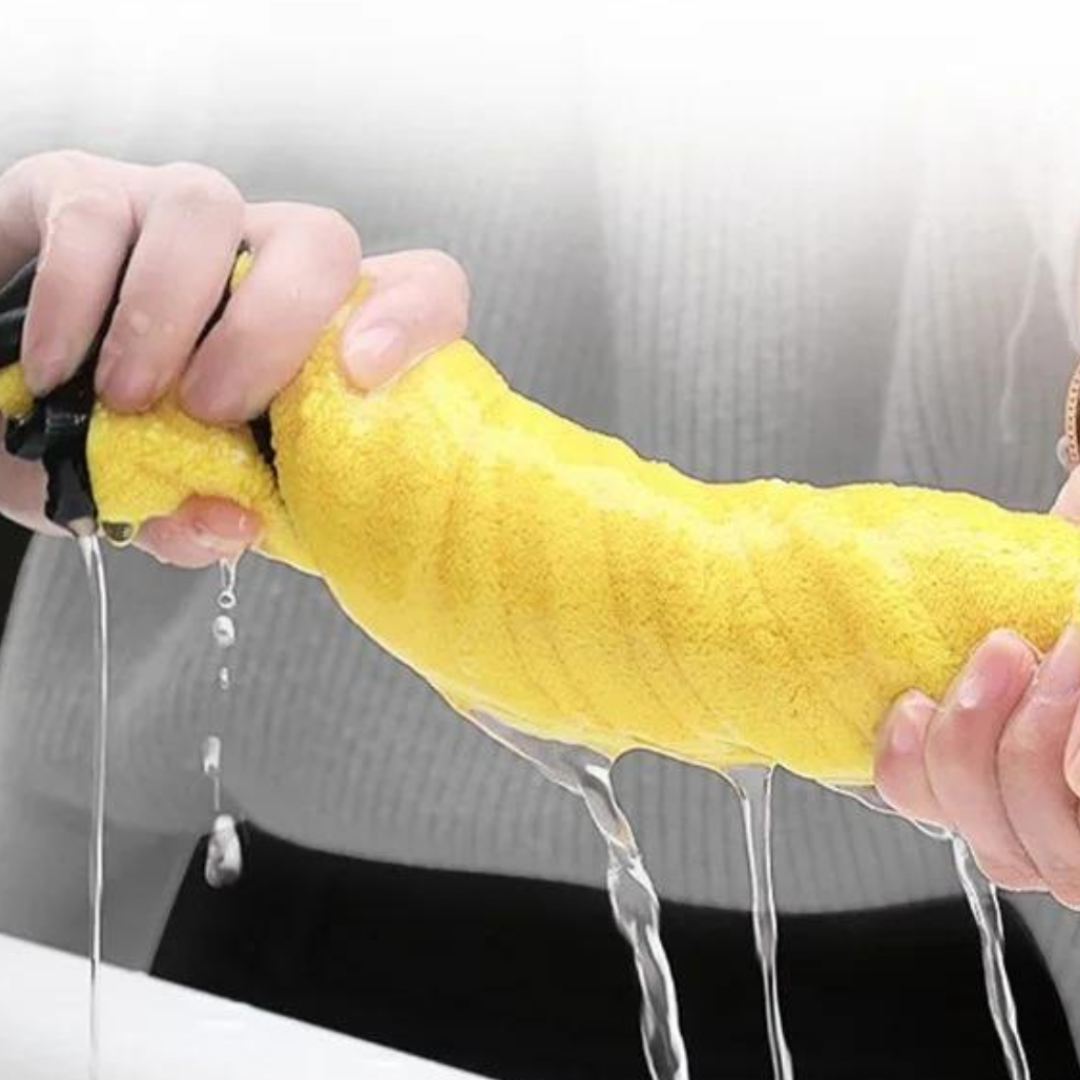 Person holding a yellow microfiber towel with water dripping from it against a neutral background