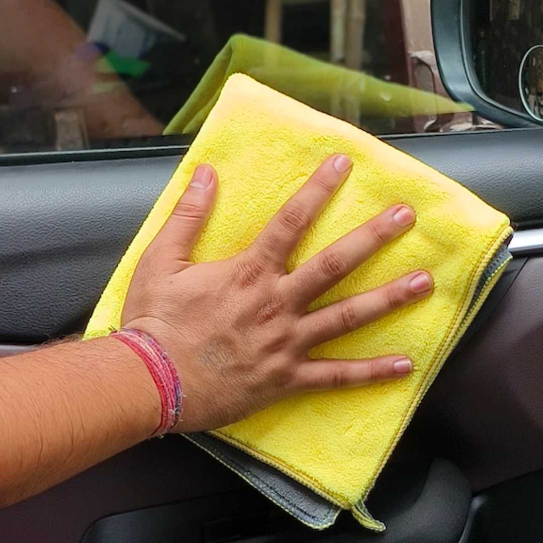 Person cleaning car interior with a yellow microfiber cloth