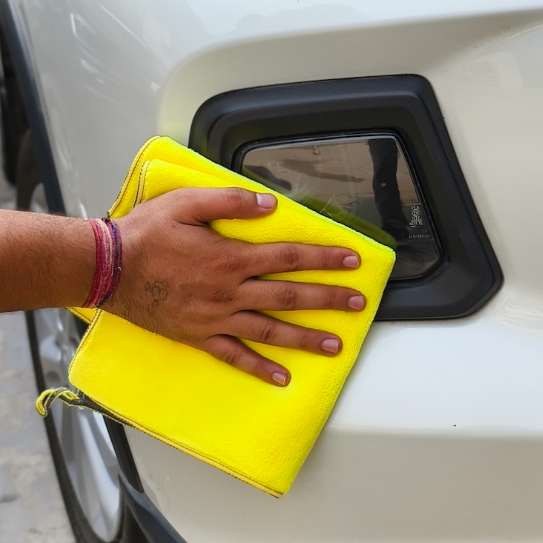 Hand holding a yellow cloth over a car's light  cap